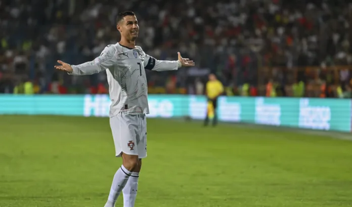 Cristiano Ronaldo celebrating on the football pitch in Portugal kit with arms outstretched.