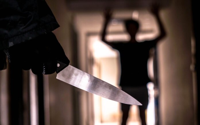 Hand with knife following young terrified in the apartment. man