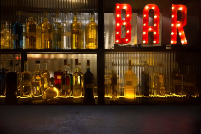 Vintage BAR sign with lights in the dark with bottles of alcohol
