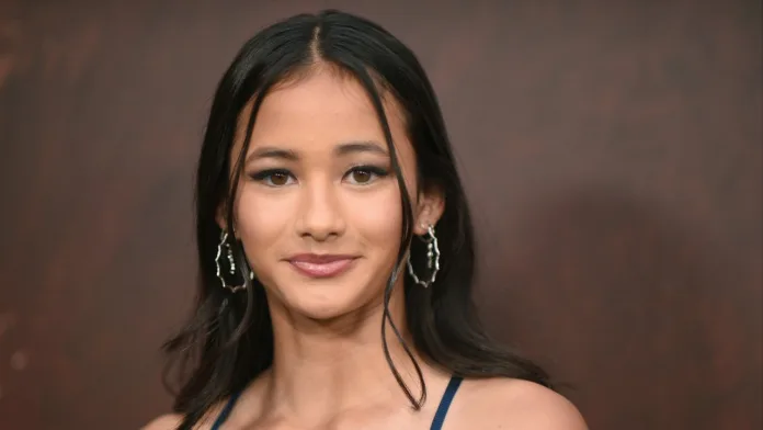 Kaylee Hottle poses for a portrait at a film premiere, wearing a blue dress and silver hoop earrings.