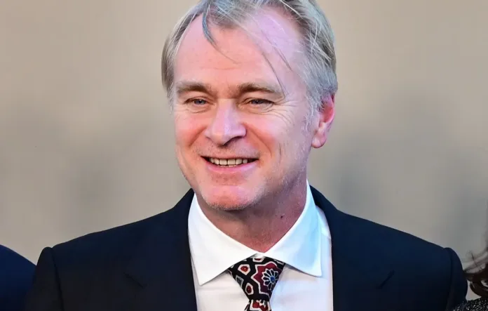 Christopher Nolan smiling while wearing a suit and patterned tie.