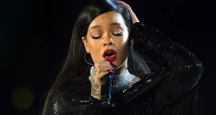 Rihanna performing live on stage while singing into a handheld microphone.