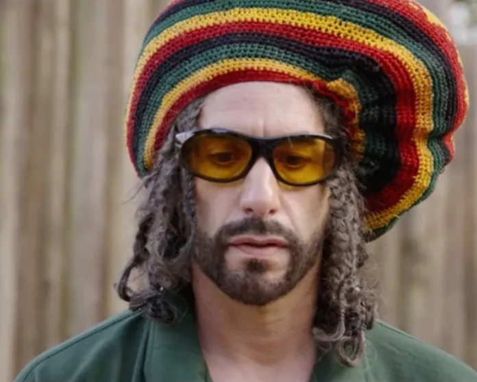 Sacha Baron Cohen as Ali G wearing a colourful striped hat, yellow-tinted sunglasses and dreadlocks in the 2026 film Ali G: Who Iz I?