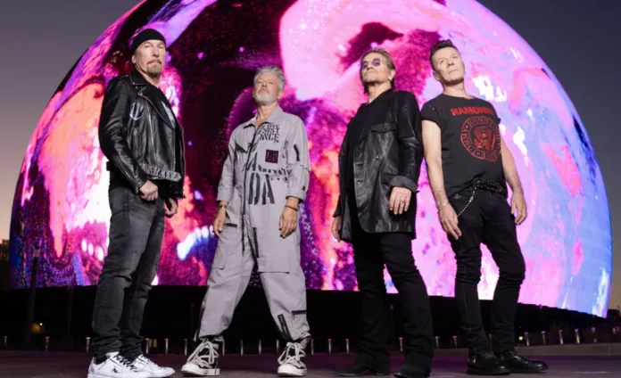 U2 band members The Edge, Larry Mullen Jr., Bono and Adam Clayton standing in front of the illuminated Sphere in Las Vegas.